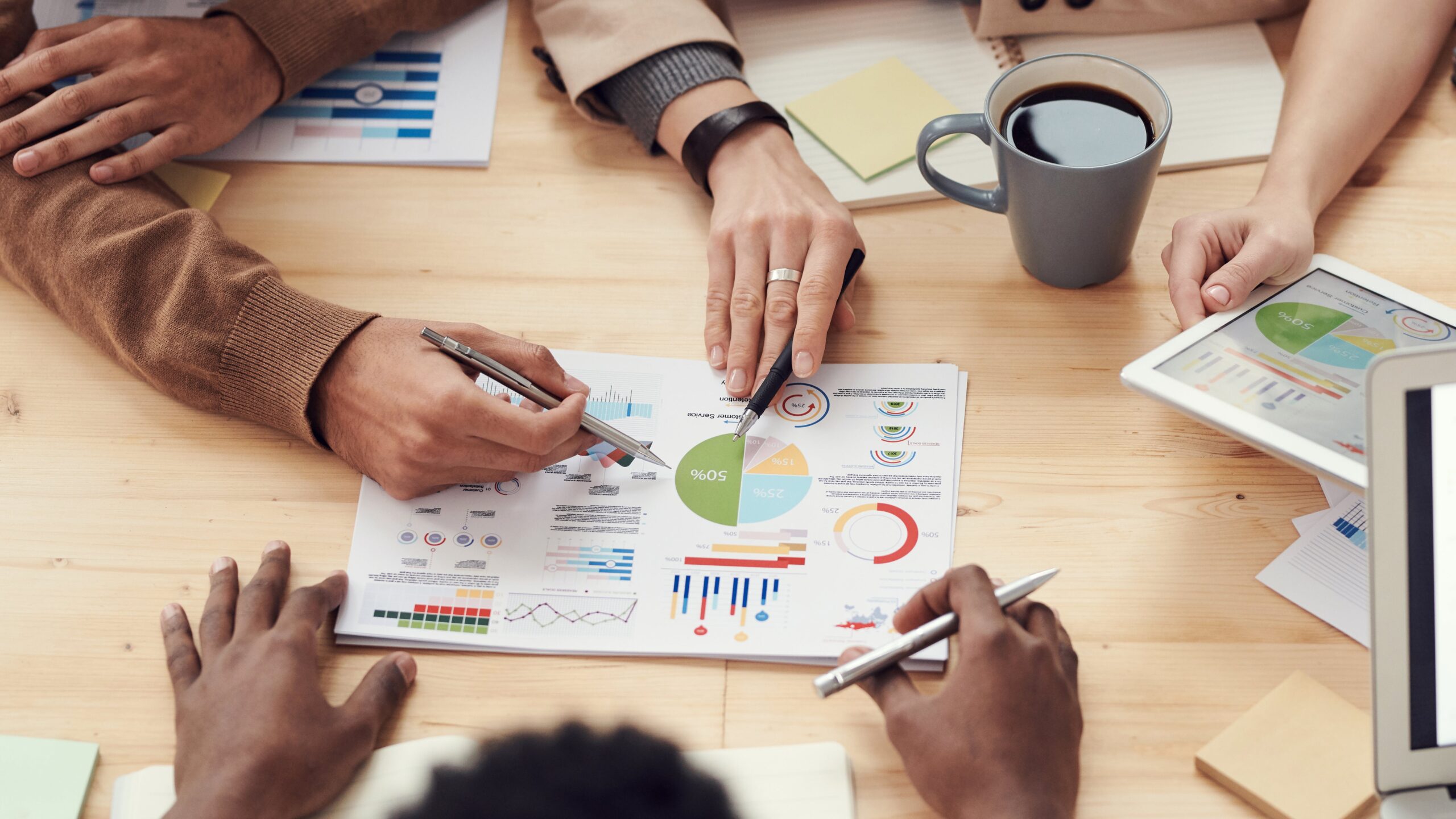 Four people sit around a table, hands engaged in examining a chart and graph, deeply involved in collaborative analysis