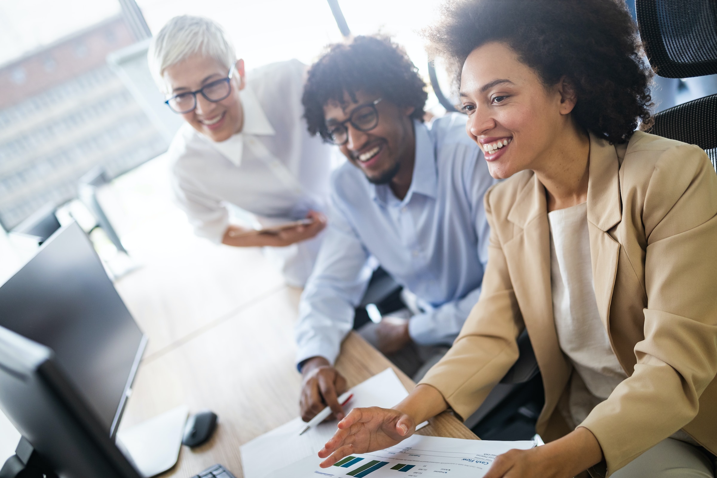 A diverse group of three happy professionals collaborating and looking at a computer, exemplifying teamwork and inclusivity in the workplace.