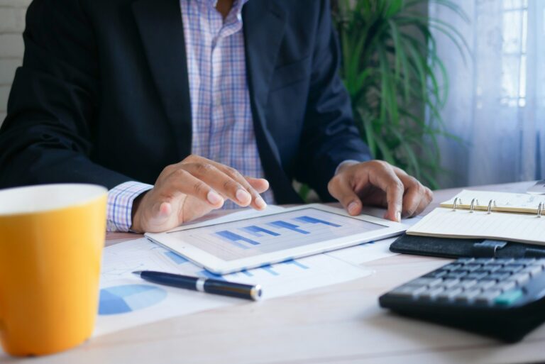 Cropped image of a business man working on a tablet that has charts on it while sitting at a desk.